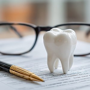 Tooth model, pen, and glasses on top of dental insurance document
